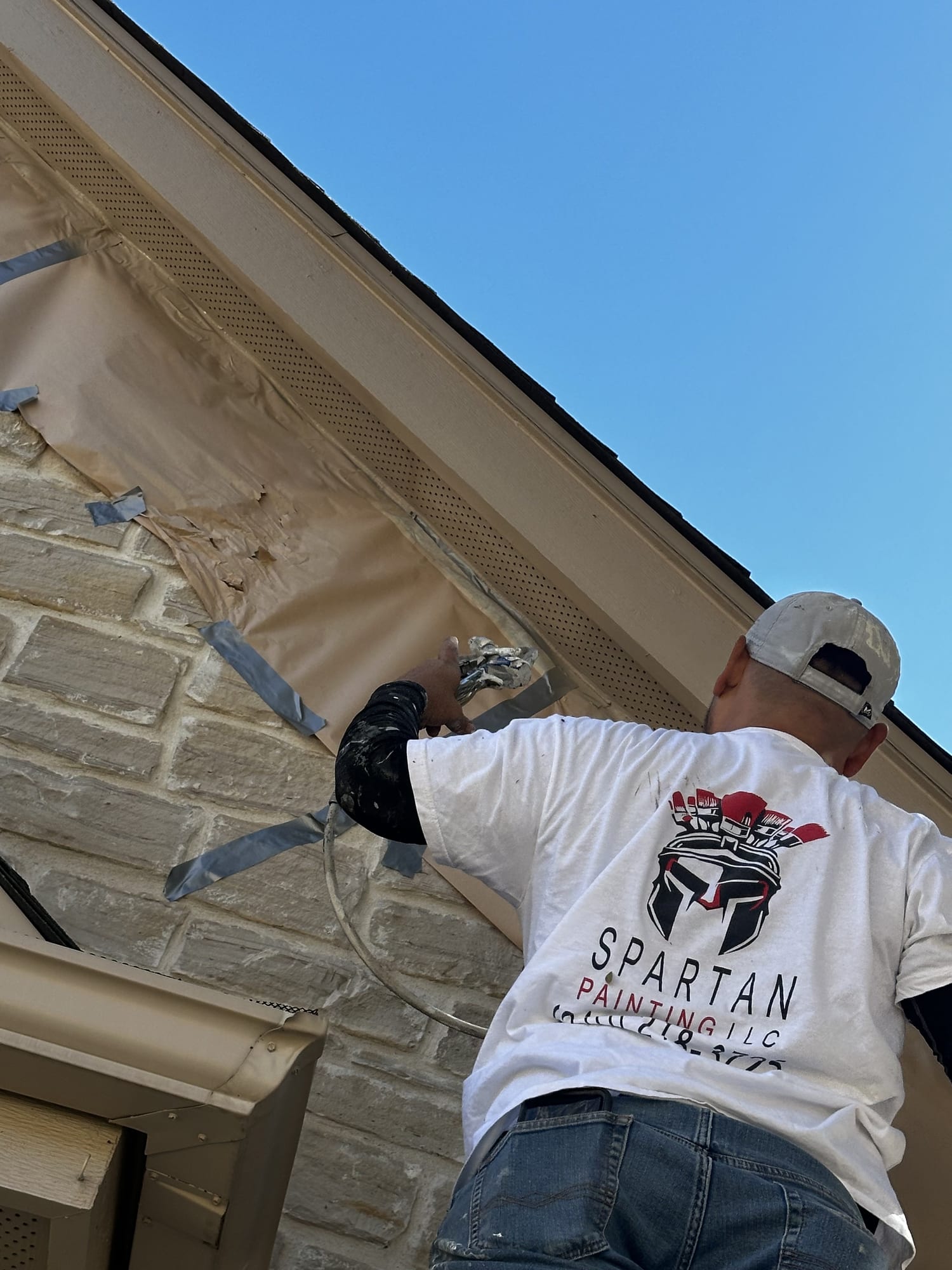 Spartan Painting crew member spraying exterior brick beneath the eaves